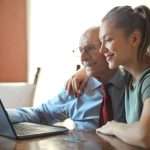 young positive woman helping senior man using laptop