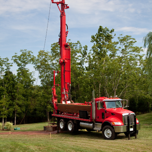 Red truck digging a well on a rural property